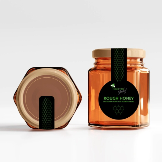 Ein Glas mit Rough Honey in sechseckigem Design. Das Etikett ist schwarz mit grünen Akzenten und zeigt die Aufschrift „Rough Honey – Deutscher Honig aus eigener Imkerei“.