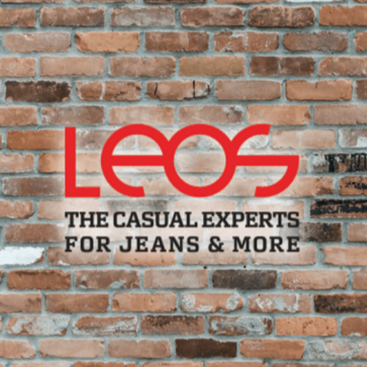 Rotes Logo von Leos auf einer Ziegelsteinwand mit dem Slogan „The Casual Experts for Jeans & More“ darunter.