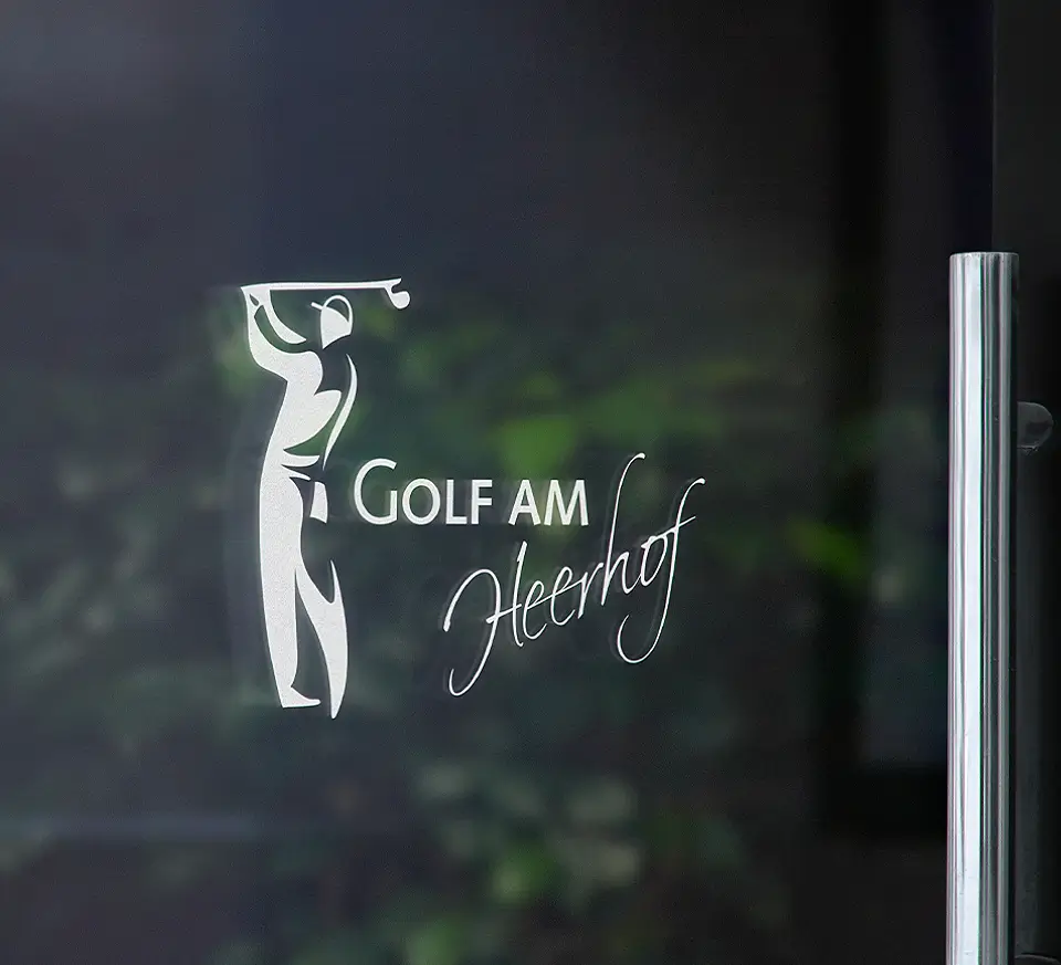 Logo des Golfparks am Heerhof auf einer Glasscheibe mit der Aufschrift 'Golf am Heerhof' und einem Golfer, der einen Abschlag macht